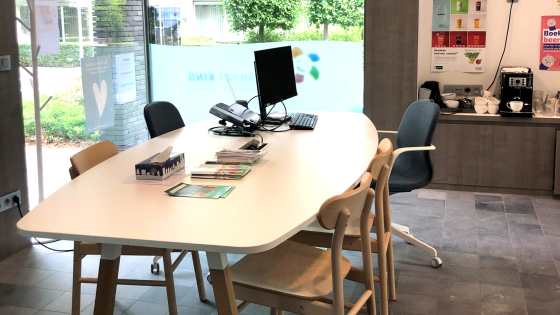 Vergaderzaal Aquarium heeft grote ramen. Er staat een ruim bureau met 5 stoelen en een computerscherm. Er is een een koffiemachine in de ruimte.