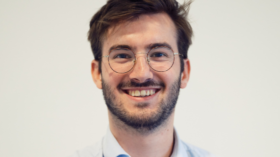Ruben heeft donker haar, een stoppelbaard en een bril. Hij draagt een lichtgrijs hemd.