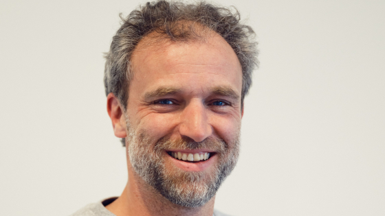 Pieter-Jan heeft bruin haar en een bruingrijs stoppelbaardje. Hij draagt een lichtgrijze trui
