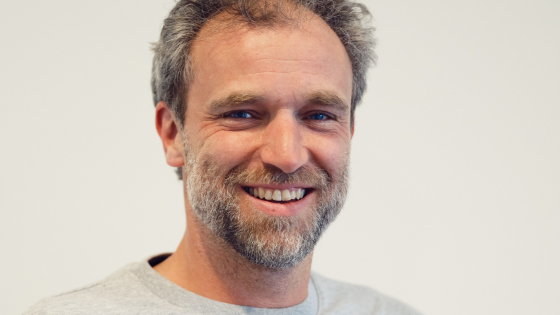 Pieter-Jan heeft bruin haar en een bruingrijs stoppelbaardje. Hij draagt een lichtgrijze trui