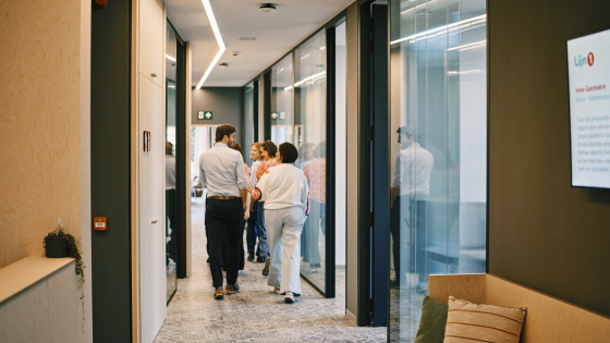 Een viertal collega's loopt door een gang. we zien hen vanop de rug