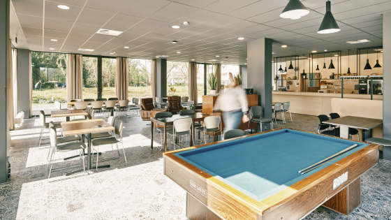 in de cafetaria staat een grote pooltafel, veel kleine tafeltjes en een bar. Er is veel licht dankzij de grote ramen