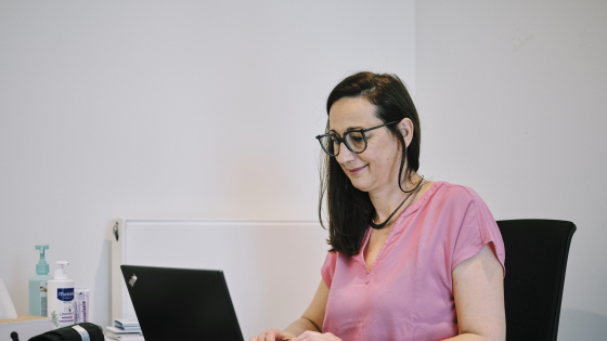 dame met een roze t-shirt zit te werken aan haar laptop
