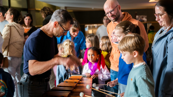 Foto van een man die uitlegt aan een jongetje hoe hij op muziekinstrument moet spelen