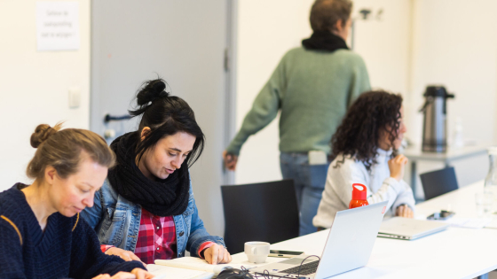 Drie vrouwen zitten aan een witte vergadertafel