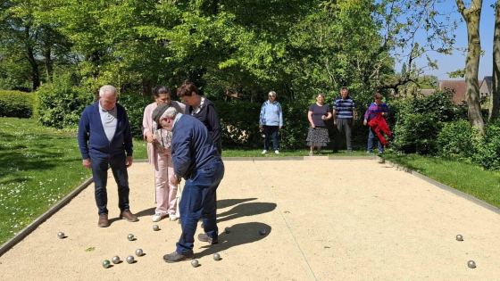 Twee teams van vier petanquespelers staan op een speelveld in de zon