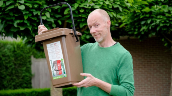 Comedian David Galle houdt een nieuwe bruine container voor keukenafval vast
