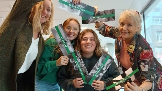 Groepsfoto van 4 vrouwen. Ze zijn vrolijk en houden een kaartje vast