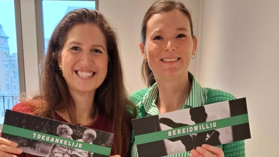 Twee vrolijke dames, ze houden kaartjes vast waarop 'toegankelijk' en 'bereidwillig' staat
