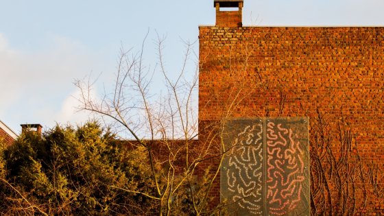 op een rode bakstenen gevel hangt een groot kunstwerk. Het werk bestaat uit twee hersenhelften. De linkerkronkels zijn groen, de rechter rood