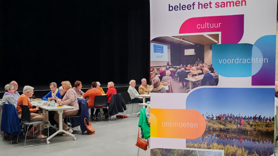 Leden van Neos aan verschillende tafels. Op de voorgrond staat een banner van NEOS