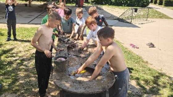 groepje kinderen staat rond een tafel buiten. Ze spelen met zand