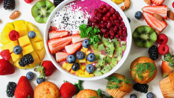 Bovenaanzicht van een tafel vol gezonde voeding: een kom met yoghurt met aardbeien, blauwe bessen, mango, kiwi en framboze