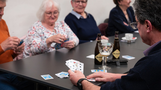 Vier mensen zitten aan tafel te kaarten. Ze drinken een goed biertje
