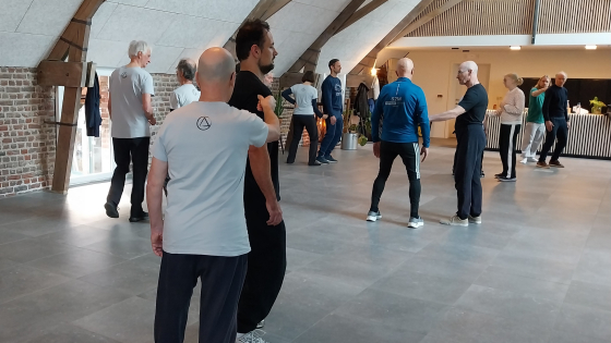 Verschillende duo's staan in een zaal. Ze hebben sportieve kleren aan voor deze activiteit