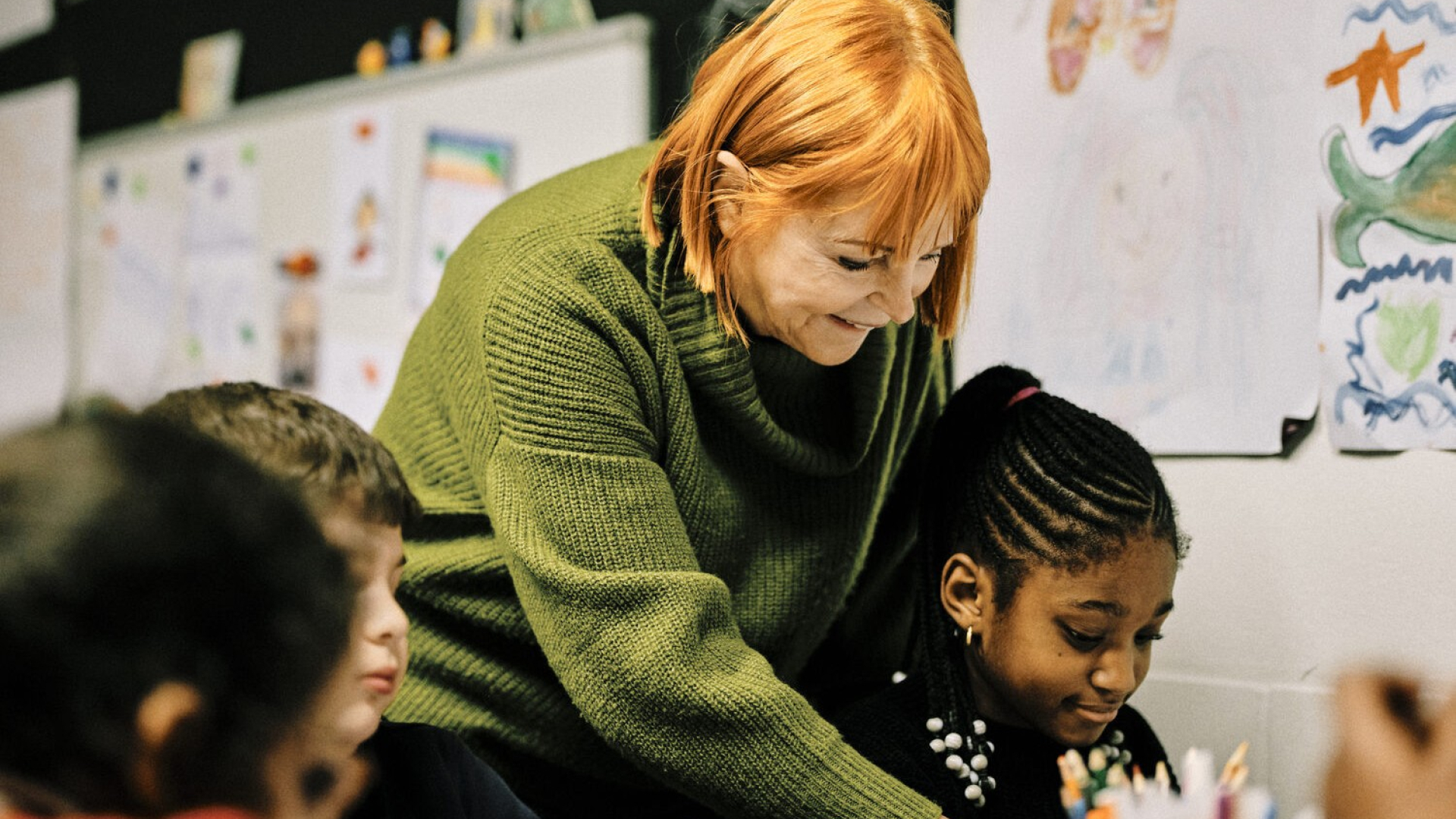 Een roodharige vrijwilliger helpt een klein meisje op school. 