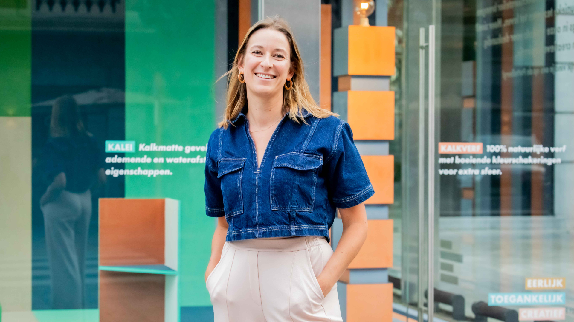 Vrouw staat met handen in zakken voor glazen muur met decoratie