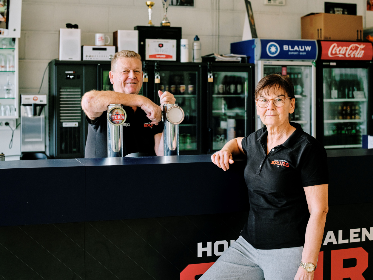Lieven staan achter de bar en leunt met zijn arm op de tap. Carine staat voor de bar