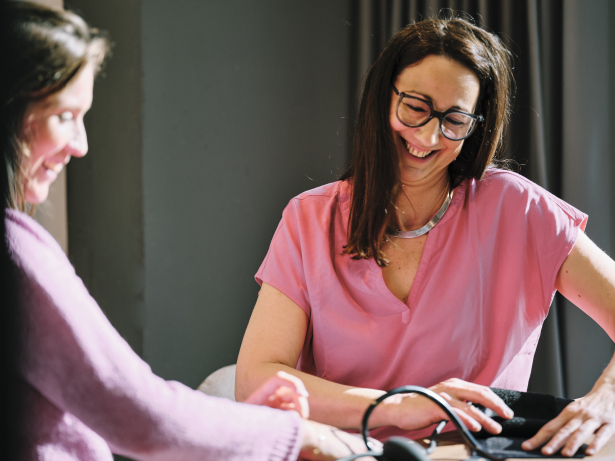 Twee vrouwen aan een tafel. De ene vrouw meet de bloeddruk van de andere vrouw