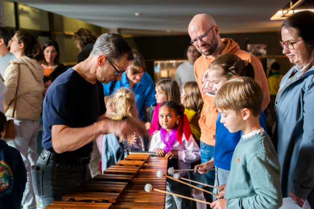 Foto van een man die uitlegt aan een jongetje hoe hij op muziekinstrument moet spelen