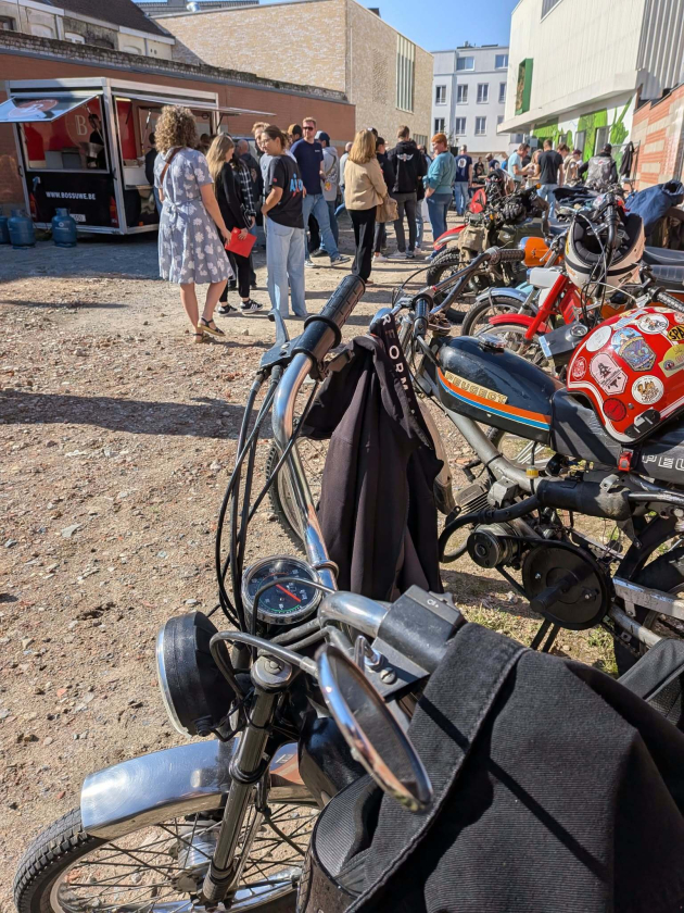 Foto van fietsen en motors op de voorgrond en mensen op achtergrond