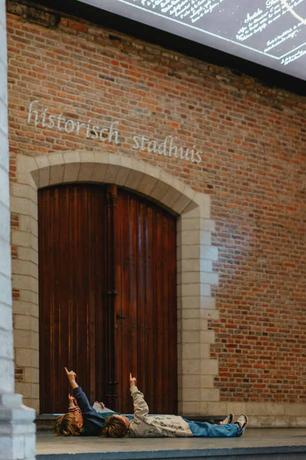 Foto van 2 kinderen die het familieparcours Kunst Publieke Ruimte volgen en de opdracht bij het Verdrag van Kortrijk uitvoeren.