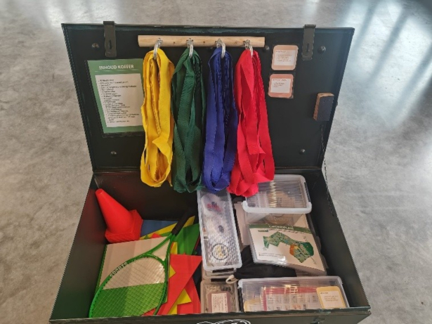 Koffer 'De Saboteur' met daarin onder andere blinddoeken, een racket, een kegel, ...