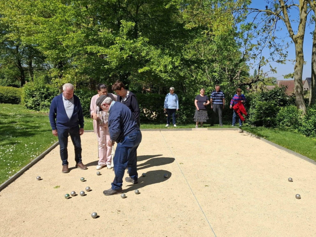 Twee teams van vier petanquespelers staan op een speelveld in de zon