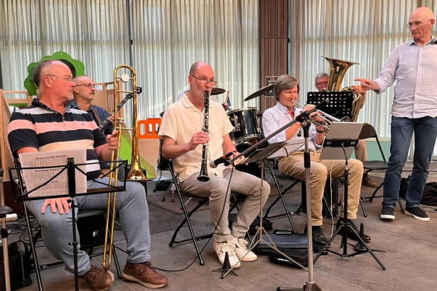 Groepsfoto. De leden van de band zitten op stoelen en hebben hun instrumenten vast: een schuiftrompet, trombone, fagot en gewone trompet