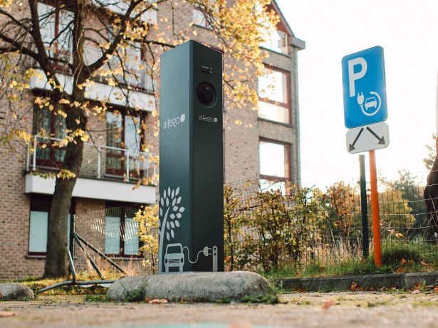 Donkergrijze elektrische laadpaal. Ervoor stat een blauw verkeersbord dat duidelijk maakt dat de parkeerplaatsen bestemd zijn voor ladende voertuigen