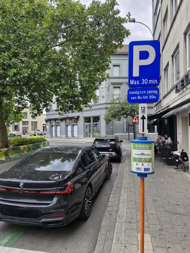 De Shop&Go-plaats is gemarkeerd met groene lijnen.  Een paal met info geeft duidelijk aan dat dit zo'n parkeerplaats is en wat de regels zijn op zo'n Shop&Go-plaats