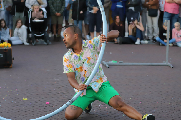 Acrobaat met een hoepel op straat. rond hem staat publiek te kijken