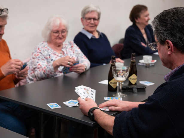 Vier mensen zitten aan tafel te kaarten. Ze drinken een goed biertje