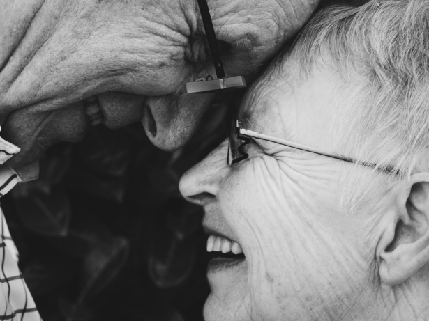 Zwart wit foto van een oudere man en vrouw. Hun voorhoofden raken en elkaar, ze lachen